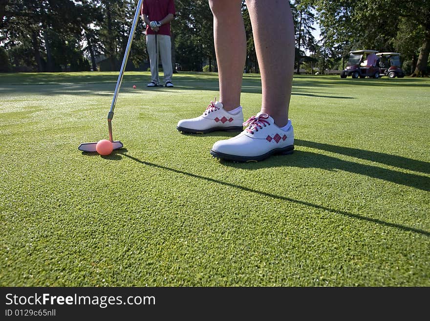 A person is standing on the green of a golf course.  They are about to putt a ball into a hole.  Horizontally framed shot. A person is standing on the green of a golf course.  They are about to putt a ball into a hole.  Horizontally framed shot.