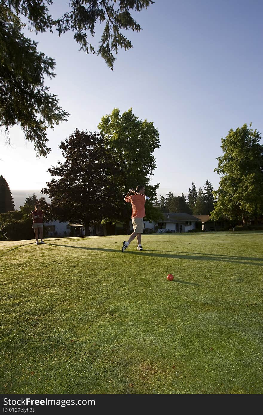 A young couple is standing on a golf course and playing golf.  The man is looking at the ball he just hit and the woman is looking at the man.  Vertically framed shot. A young couple is standing on a golf course and playing golf.  The man is looking at the ball he just hit and the woman is looking at the man.  Vertically framed shot.