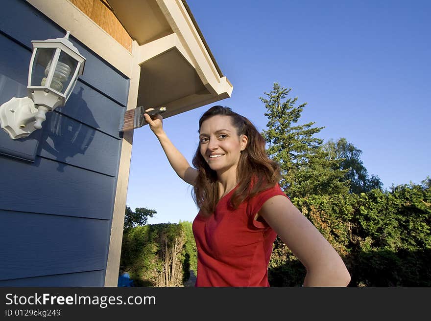 Woman smiling as she paints her house. Horizontally framed photograph. Woman smiling as she paints her house. Horizontally framed photograph.