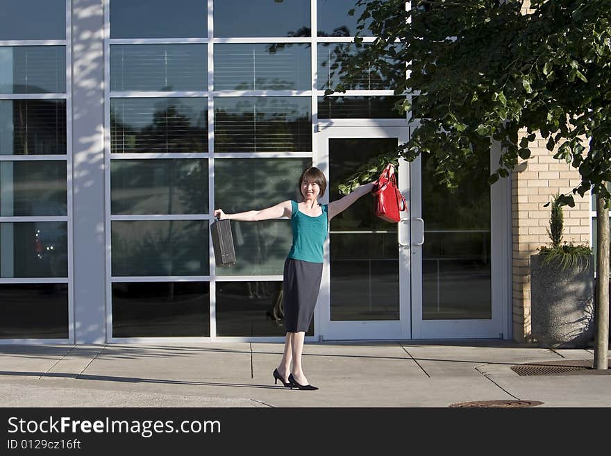 Woman smiles at camera while holding briefcase and red handbag out to her side. Horizontally framed photo. Woman smiles at camera while holding briefcase and red handbag out to her side. Horizontally framed photo.