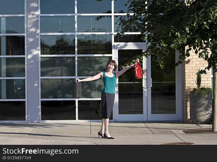 Woman smiles at camera while holding briefcase and red handbag out to her side. Horizontally framed photo. Woman smiles at camera while holding briefcase and red handbag out to her side. Horizontally framed photo.