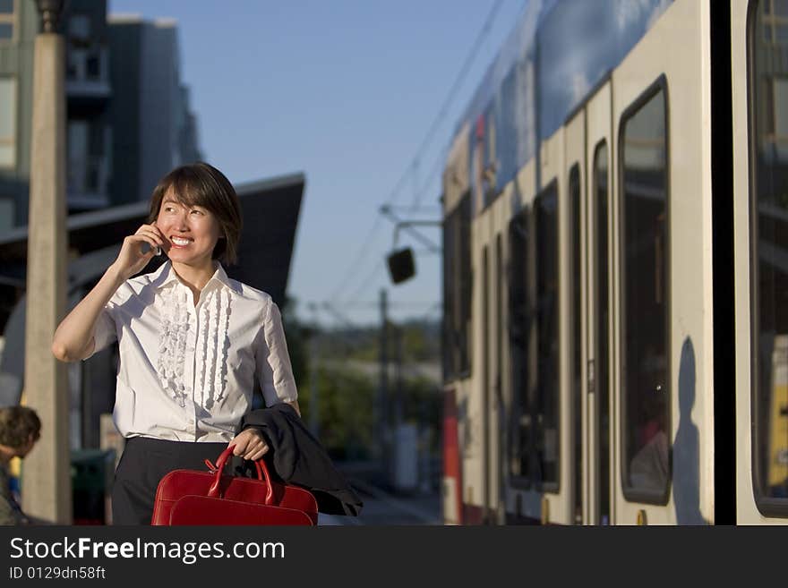 Smiling woman walks while talking on cell phone and holding red handbag. She is walking next to a train. Horizontally framed photo. Smiling woman walks while talking on cell phone and holding red handbag. She is walking next to a train. Horizontally framed photo.