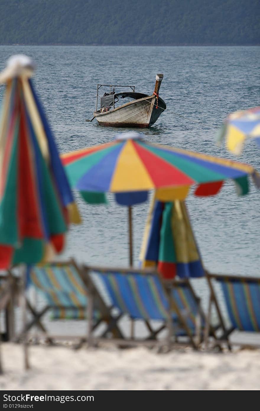 Colorfully sun beds, umbrellas and fishing boat in an island. Colorfully sun beds, umbrellas and fishing boat in an island