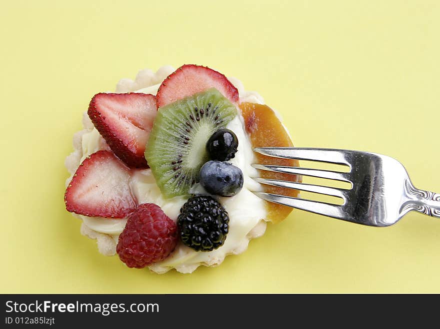 Cream-filled pastry tart topped with an assortment of juicy berries, kiwi, and peach. A silver fork stands ready to enjoy the gourmet treat. Cream-filled pastry tart topped with an assortment of juicy berries, kiwi, and peach. A silver fork stands ready to enjoy the gourmet treat.