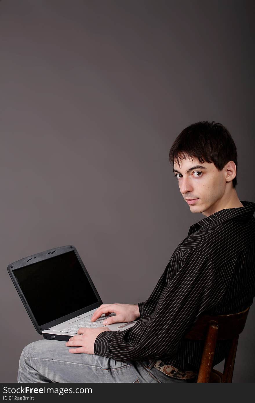 Casual young man sitting with laptop/ Dark bakground