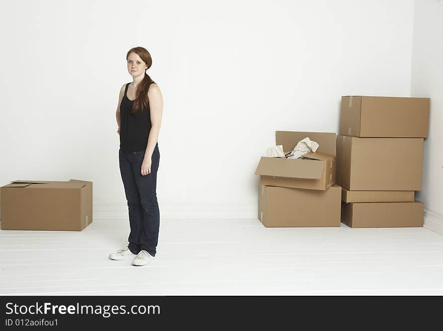 Young red headed woman standing in white room with moving boxes to both sides. Young red headed woman standing in white room with moving boxes to both sides.