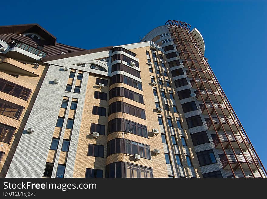 New modern brick multistory house on deep blue sky background in three colors: red, yellow, grey.