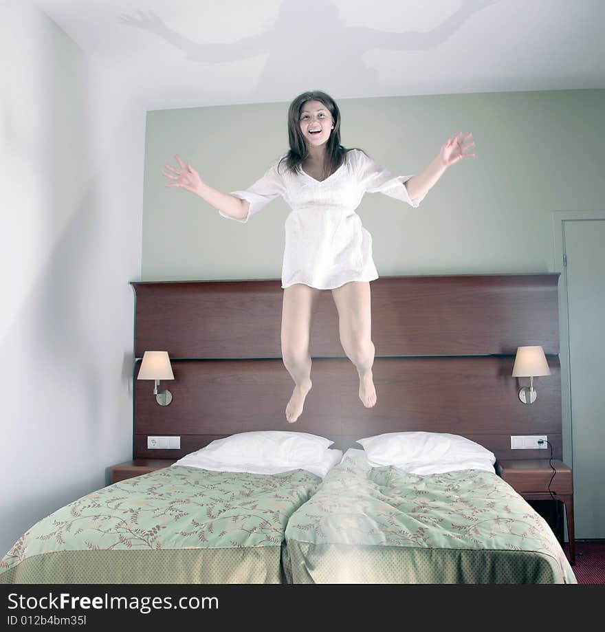 Happy young girl jumping on bed in hotel room, selective focus on face, hands and legs motion blurred. Happy young girl jumping on bed in hotel room, selective focus on face, hands and legs motion blurred