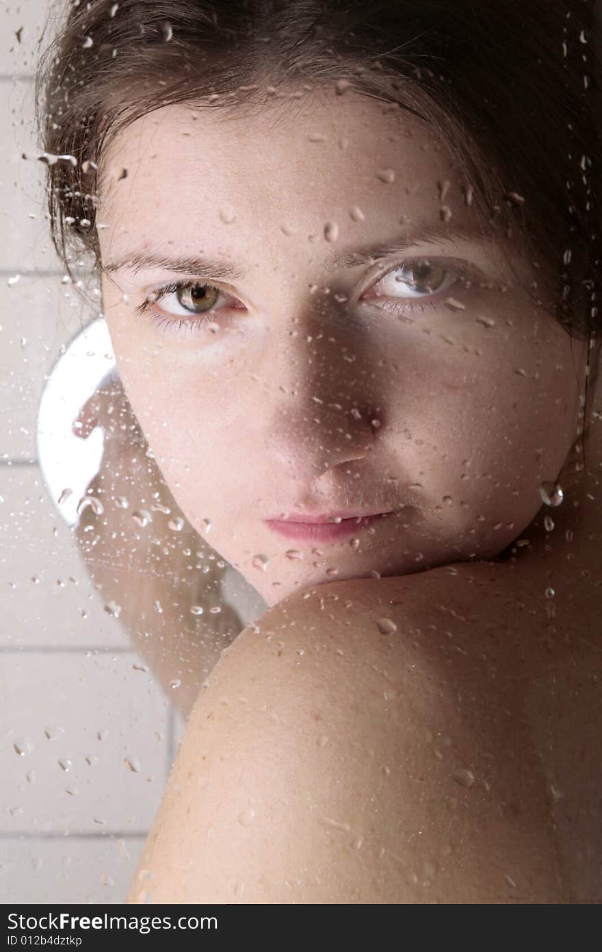 Young woman looking through the cabin shower glass with water drops on it. Young woman looking through the cabin shower glass with water drops on it