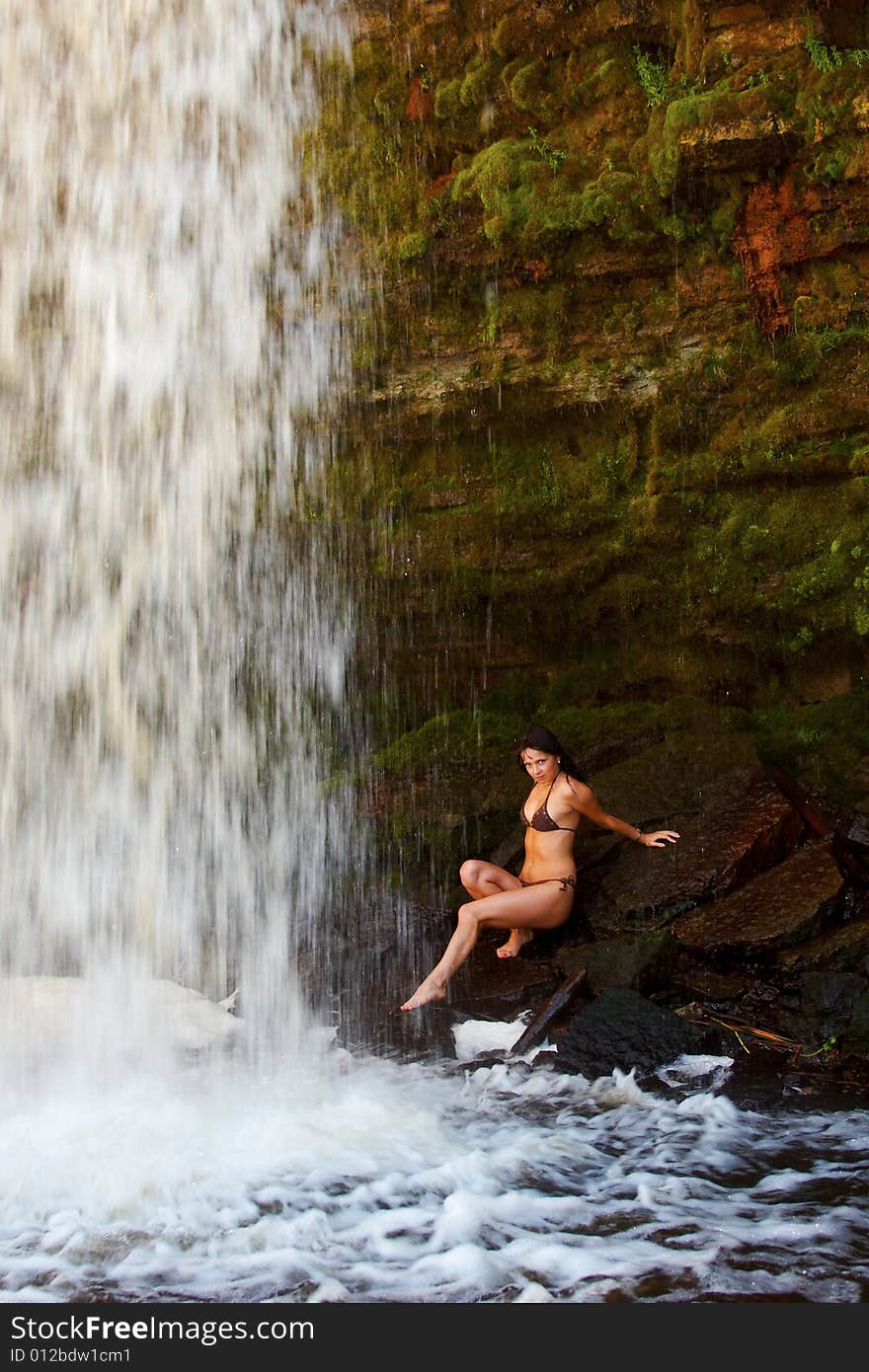 Young lady in bikini posing on stones near waterfalls. Young lady in bikini posing on stones near waterfalls