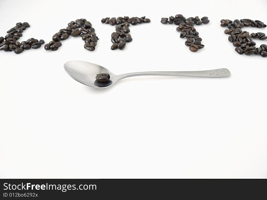 Word latte spelled with coffee beans; focus is on spoon and bean at foreground; copy space below