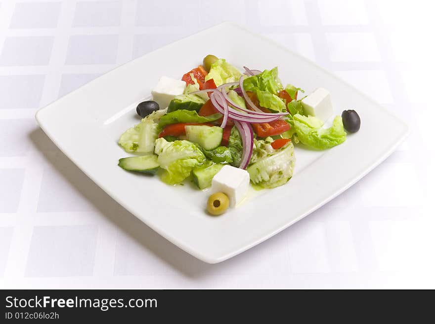 Greek Salad with vegetables, herbs and feta cheese on white plate