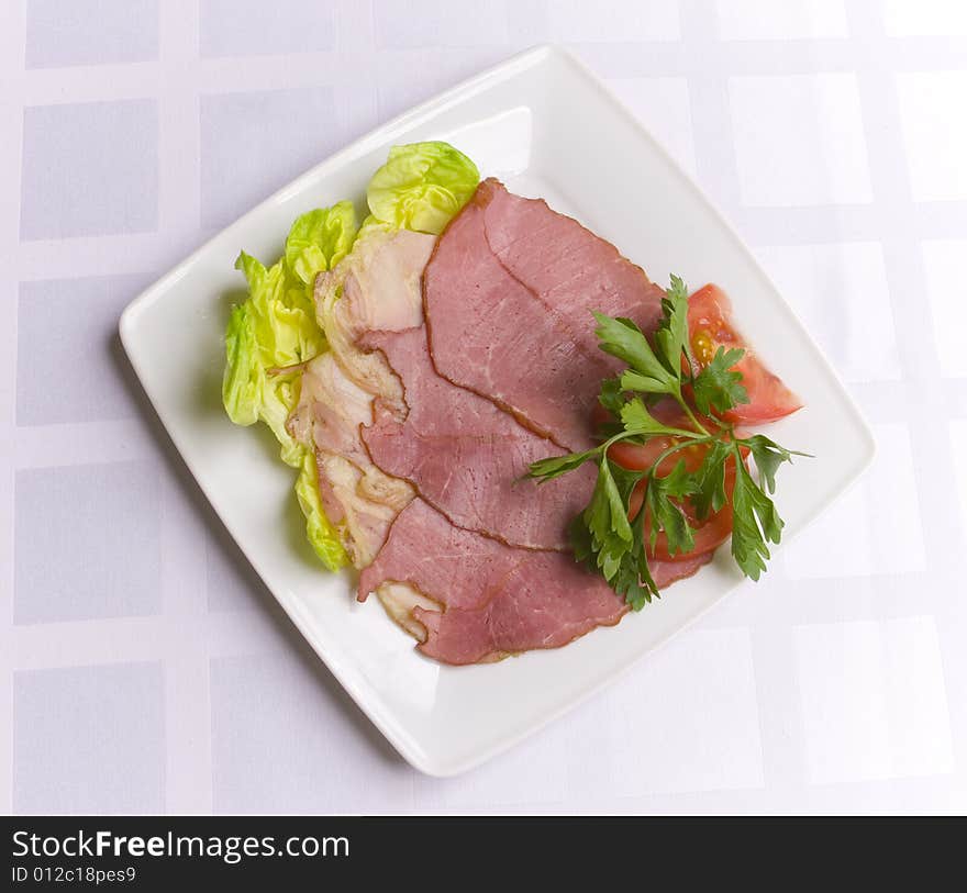 Ham decorated with salad, tomato and parsley on white plate