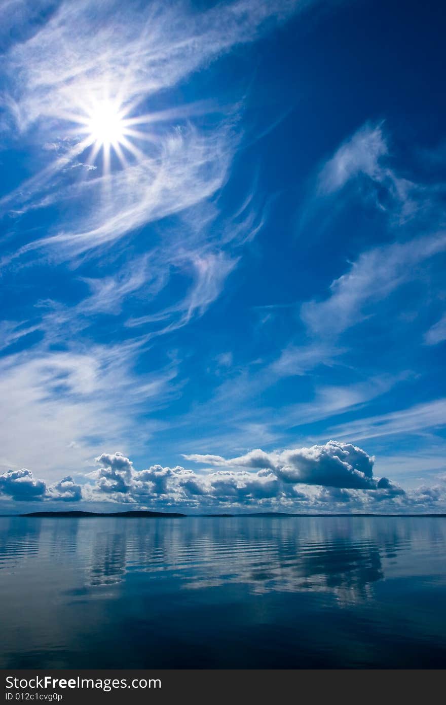 Rays of sun on bright blue sky with fluffy clouds with reflection on lake. Srednee Kuyto Lake, Karelia, Russia. Rays of sun on bright blue sky with fluffy clouds with reflection on lake. Srednee Kuyto Lake, Karelia, Russia