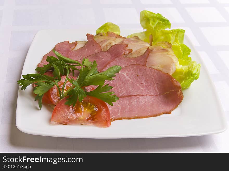 Ham decorated with salad, tomato and parsley on white plate