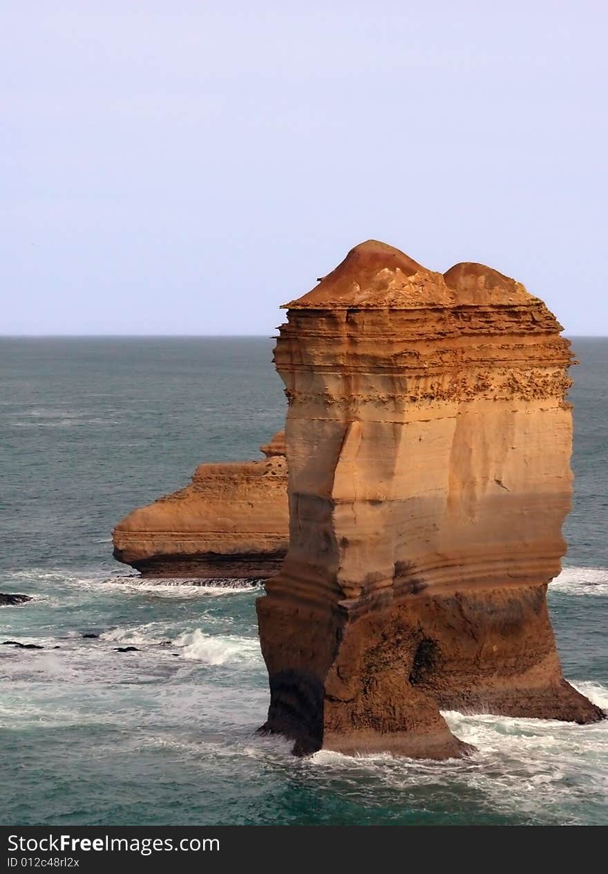 Large cliff remnant in ocean with visible layering of rock and green ocean. Large cliff remnant in ocean with visible layering of rock and green ocean