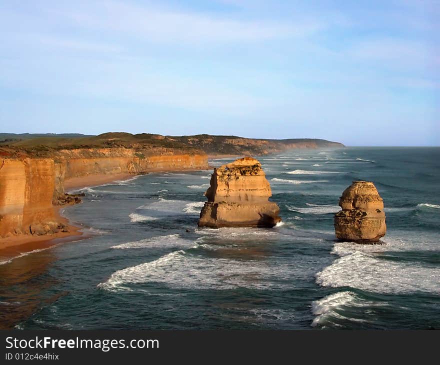 View of coastal cliffs and remnants in the ocean with blue sky and breaking waves