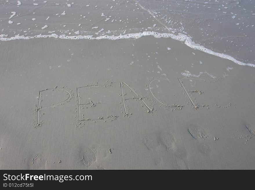 The word peace written in the sand with the water advancing on it.