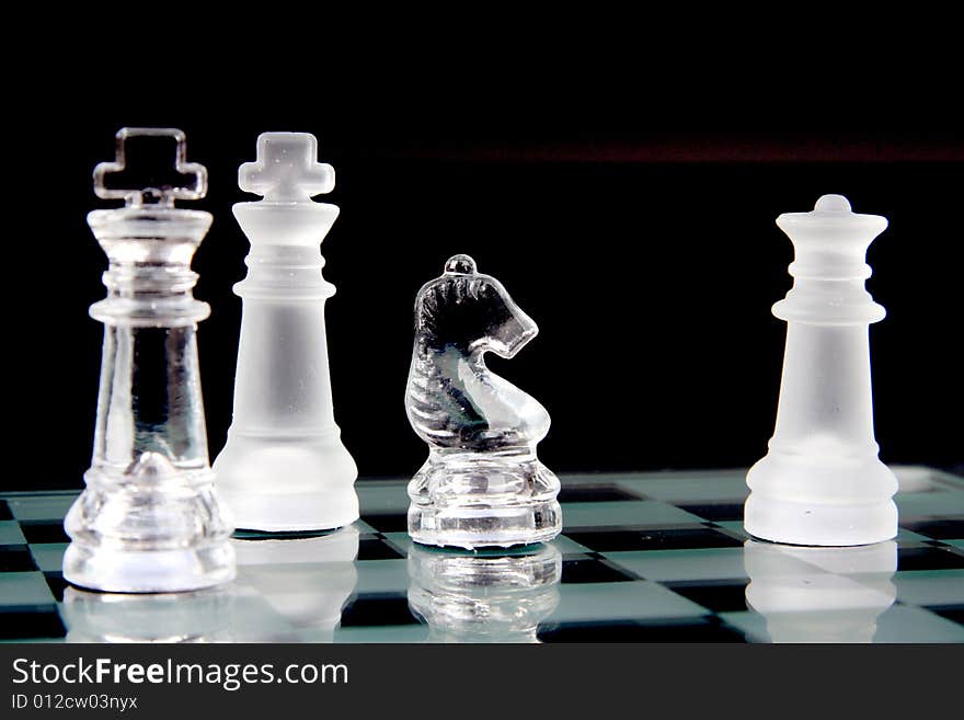 Glass chessmen on a chessboard over black background