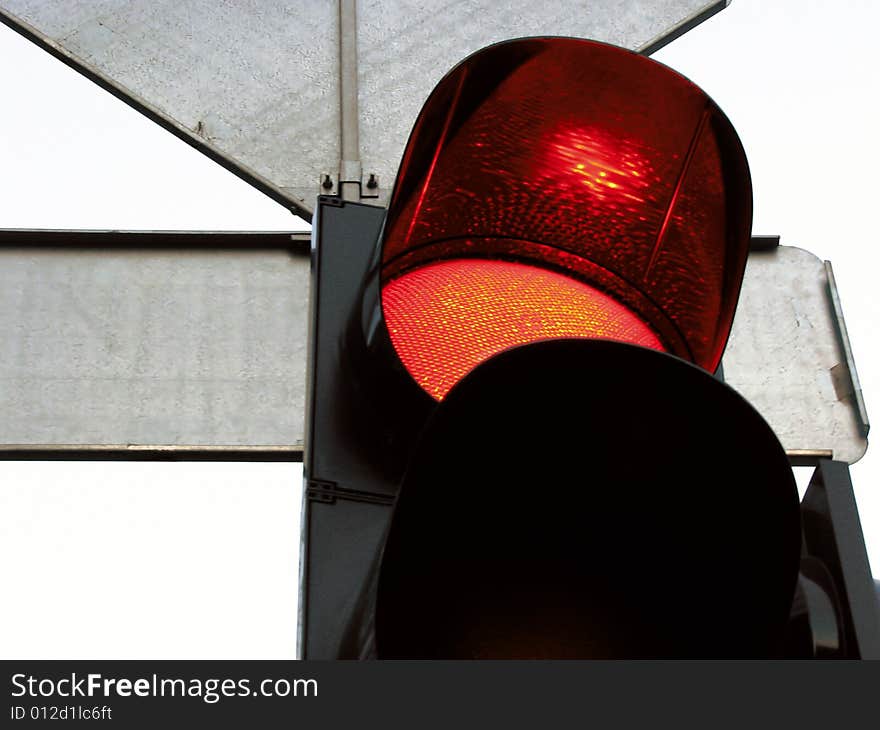 Red signal under a cap of a traffic light and a back of traffic signs. Red signal under a cap of a traffic light and a back of traffic signs