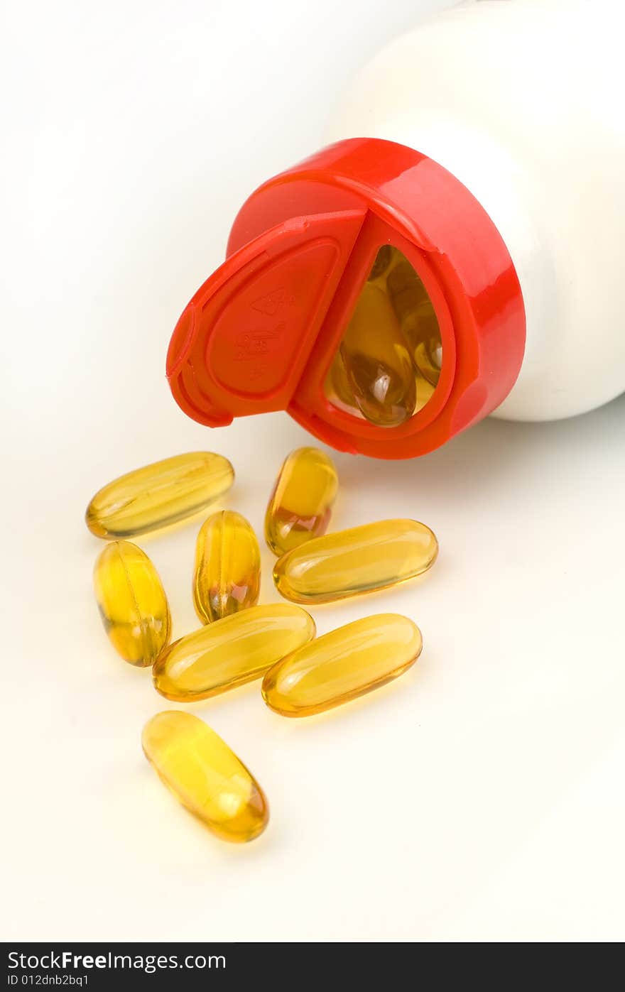 vitamin capsules spilling out of a white bottle on a white background