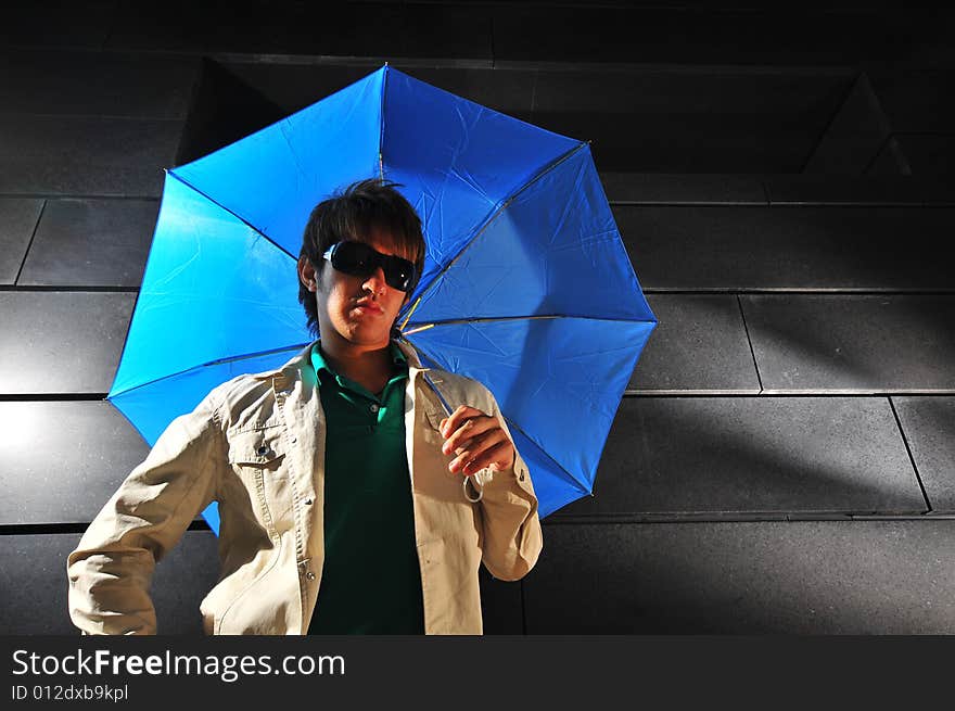 Picture of a male model with a dark background and blue umbrella. Picture of a male model with a dark background and blue umbrella.