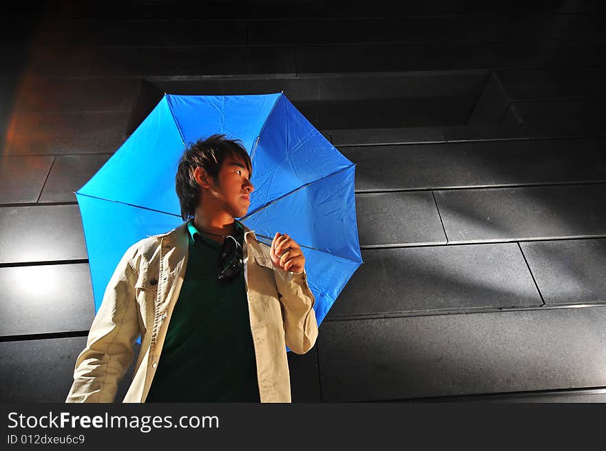 Picture of a male model with a dark background and blue umbrella. Picture of a male model with a dark background and blue umbrella.