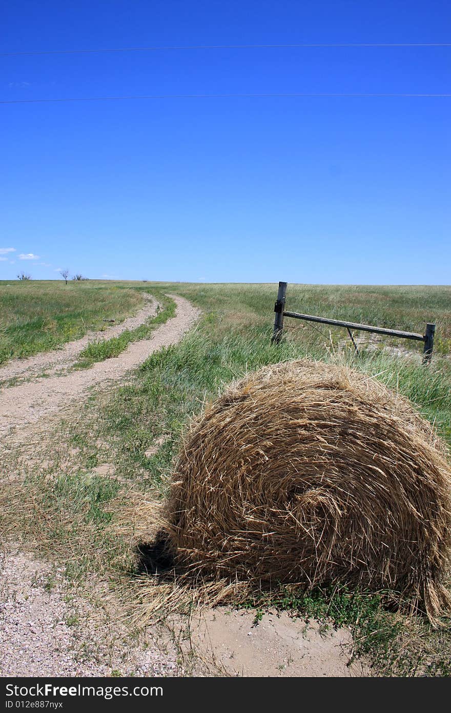 Cylindrical staw bale lies next to a field road and gate. Cylindrical staw bale lies next to a field road and gate