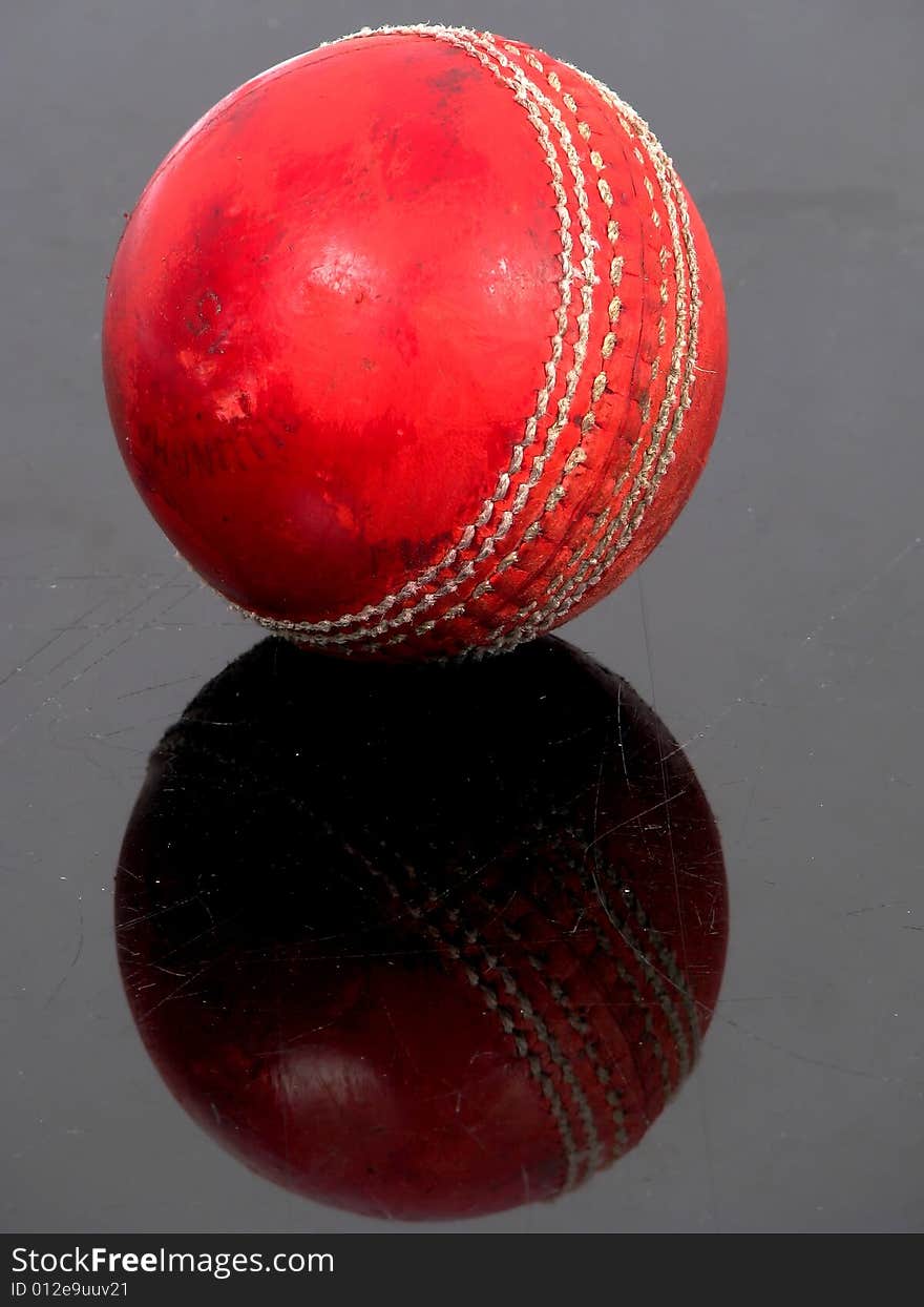 Red cricket ball on a black shiny surface. Red cricket ball on a black shiny surface