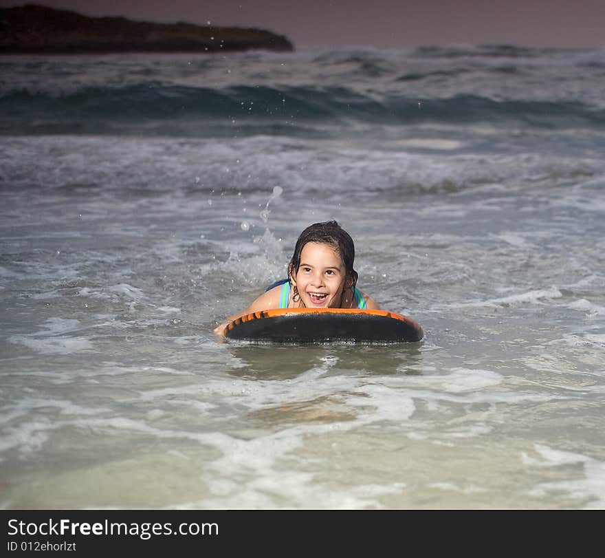 Wet young girl with boogie surf board on beach at sunset. Wet young girl with boogie surf board on beach at sunset