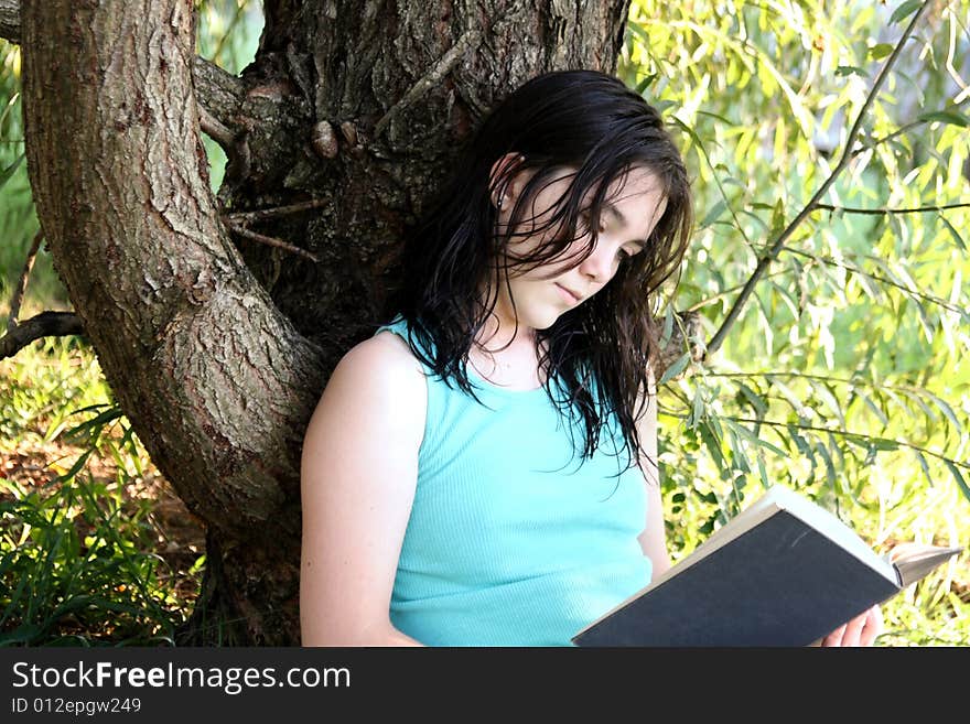 Young woman reading a book under a tree