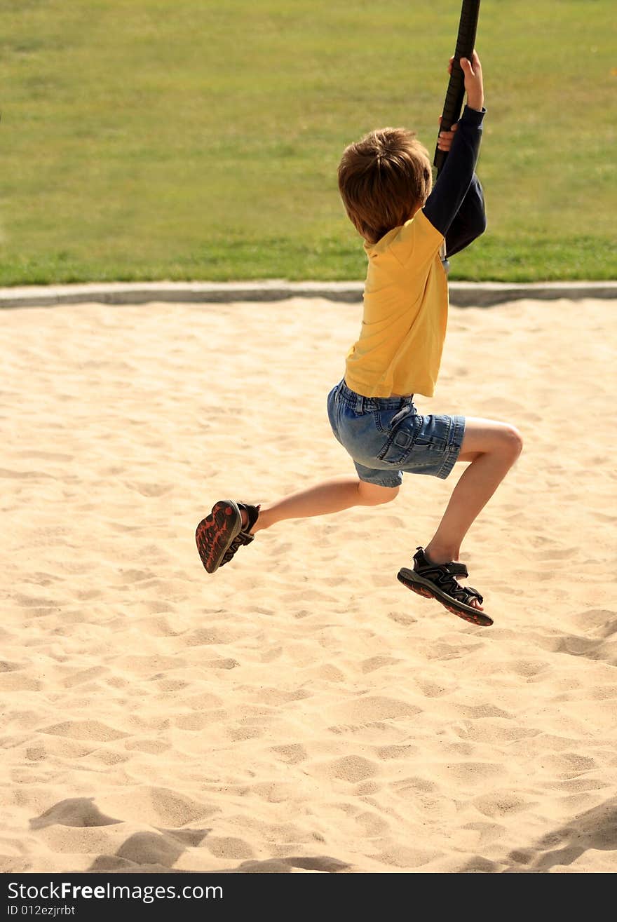 A young boy swinging from a rope on some playground equipment. A young boy swinging from a rope on some playground equipment