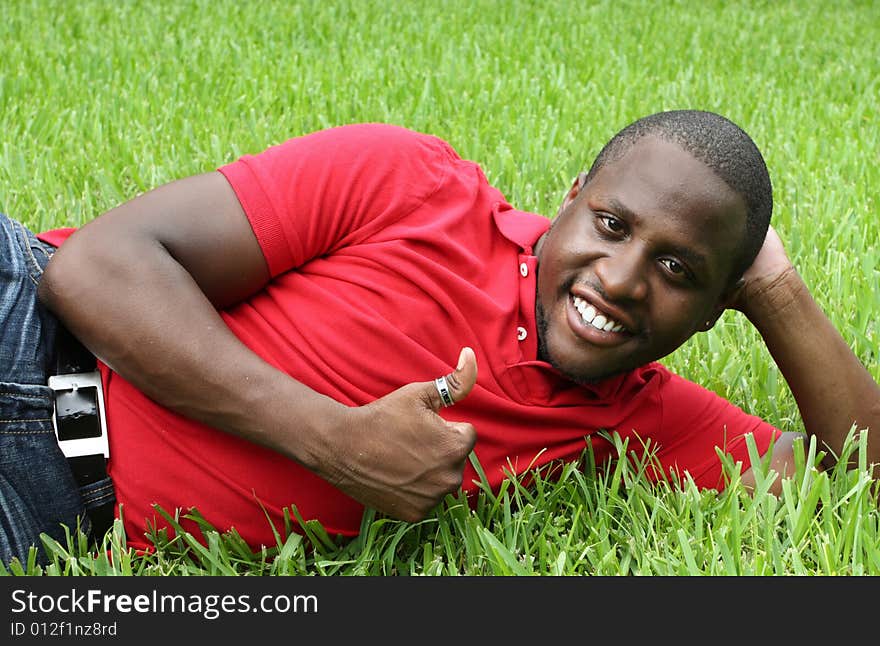 Man laying on the grass smiling and showing a thumbs up gesture. Man laying on the grass smiling and showing a thumbs up gesture.