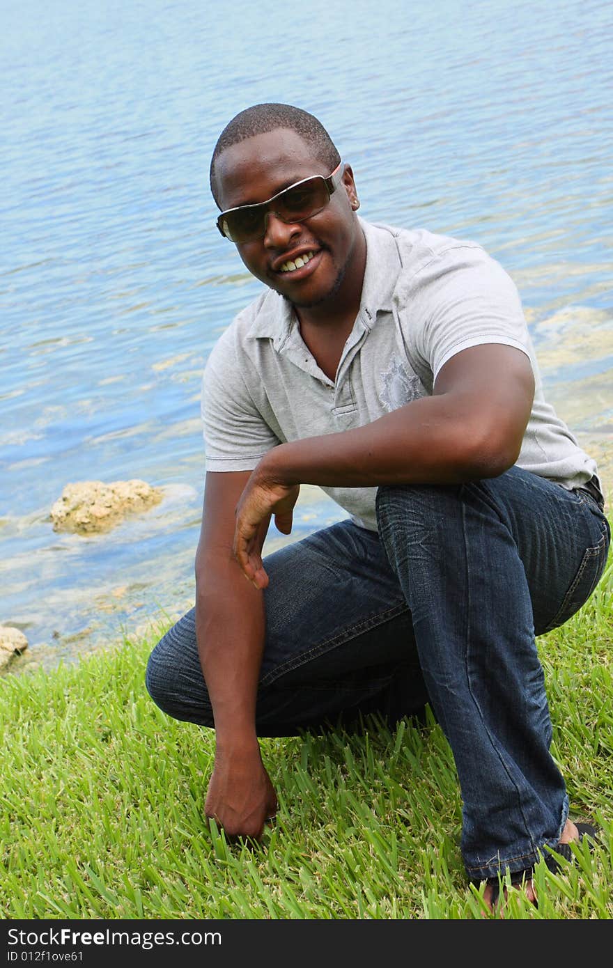 Young stylish male squatting near a pond. Young stylish male squatting near a pond