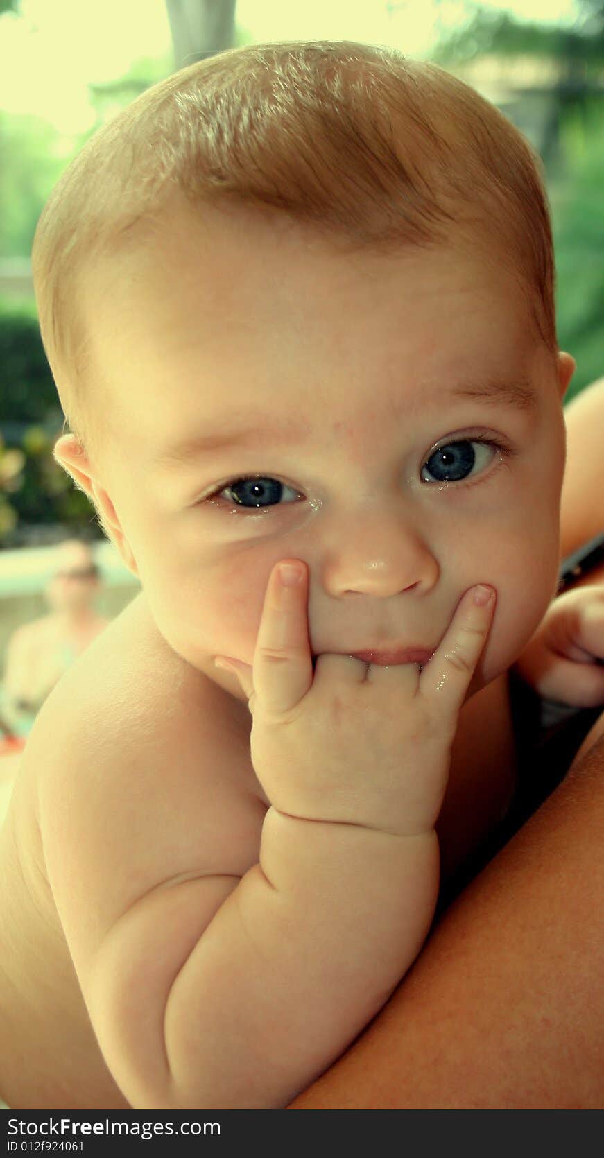 Outdoors shot of a four month old baby being held in arms, sucking on his two middle fingers (forming the rock n roll sign), looking into camera with blue eyes. Outdoors shot of a four month old baby being held in arms, sucking on his two middle fingers (forming the rock n roll sign), looking into camera with blue eyes