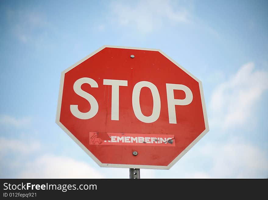 Stop sign with sticker against blue sky with clouds