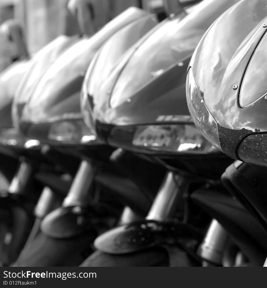 6 black motorbikes parked in a row, focus is on the front bike. 6 black motorbikes parked in a row, focus is on the front bike