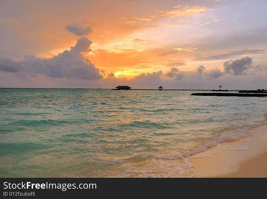 Small wave gently swapping on golden tropical beach. in the background a great sunrise or sunset is taking place. Small wave gently swapping on golden tropical beach. in the background a great sunrise or sunset is taking place.