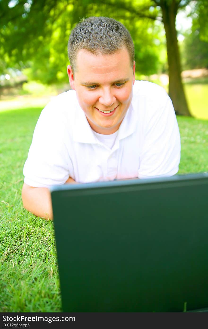 Handsome caucasian man using computer outdoor in grassy park. Handsome caucasian man using computer outdoor in grassy park