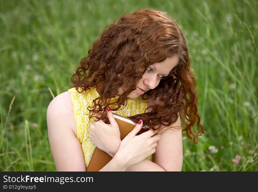 The girl with long hair presses to a breast the book on a background of a lawn. The girl with long hair presses to a breast the book on a background of a lawn