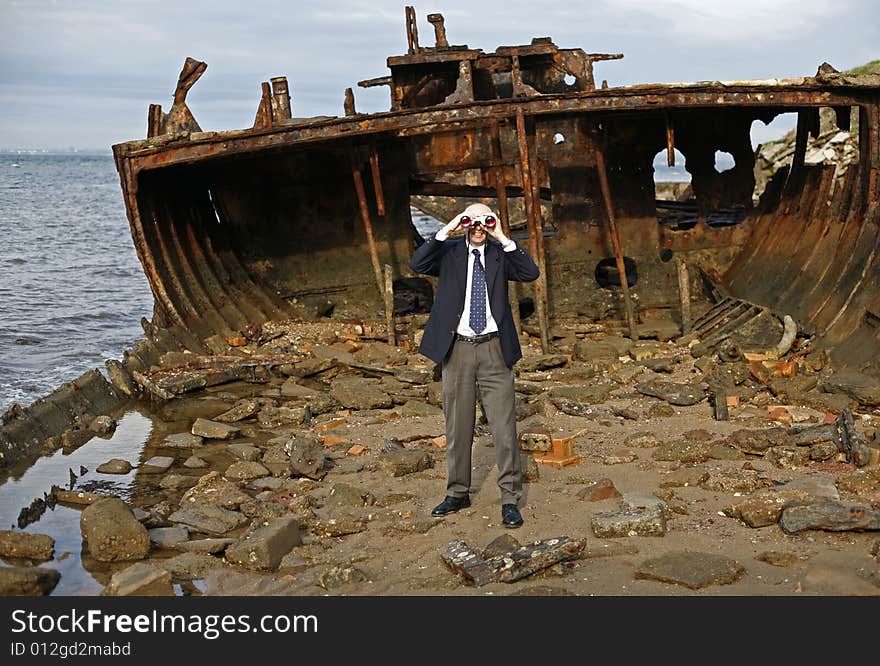 Businessman in the rusting hull of shipwreck, with binoculars looking out to the horizon, asking the question is their an escape from a sinking business. Businessman in the rusting hull of shipwreck, with binoculars looking out to the horizon, asking the question is their an escape from a sinking business