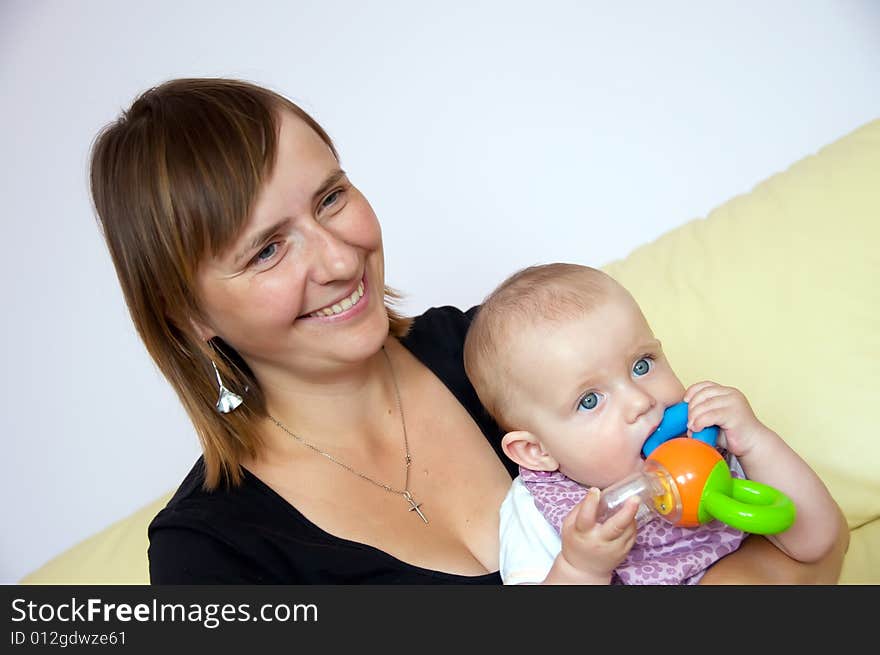 Happy mother with baby in her arms sitting on sofa. Baby is playing with a toy. Happy mother with baby in her arms sitting on sofa. Baby is playing with a toy.