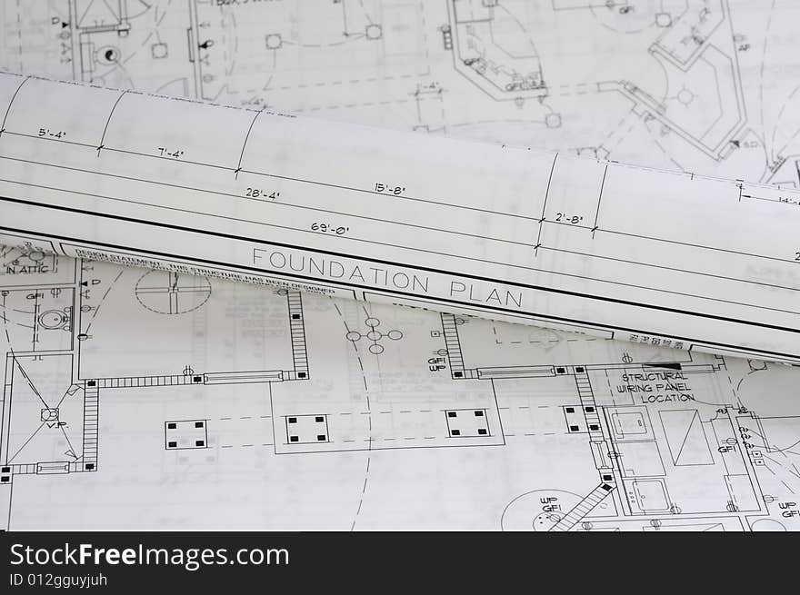 A crisp white blueprint rolled up on top of a foundation plan. A crisp white blueprint rolled up on top of a foundation plan.