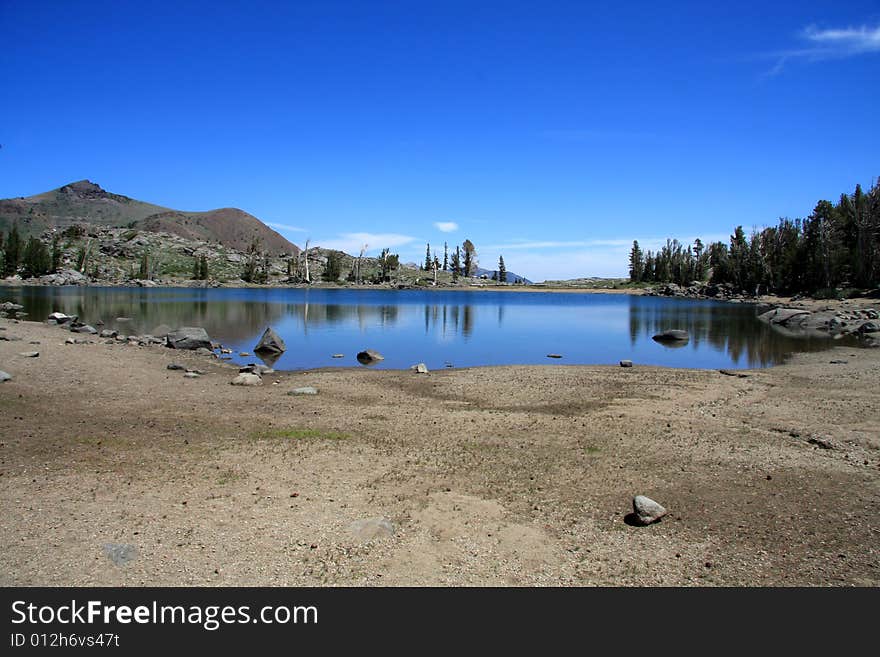 Image of low level of water in a small mountain lake, against a very blue sky. Image of low level of water in a small mountain lake, against a very blue sky.