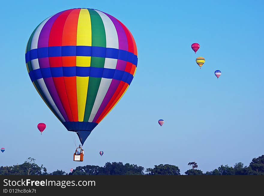 Rainbow colored hot air balloon flying just above treetop level. Rainbow colored hot air balloon flying just above treetop level