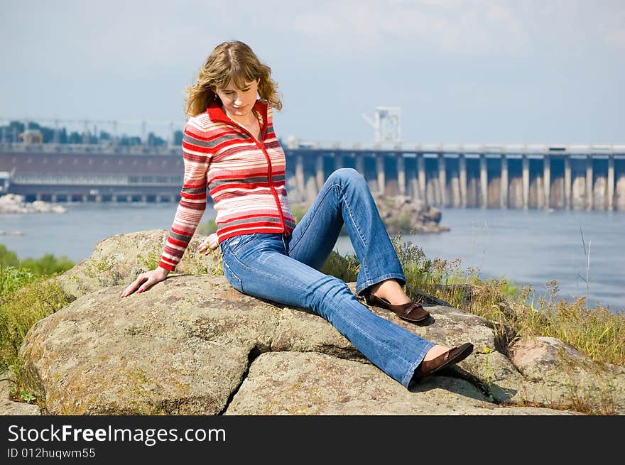 The girl sits on stones against hydroelectric power station. Zaporozhye. Ukraine. The girl sits on stones against hydroelectric power station. Zaporozhye. Ukraine