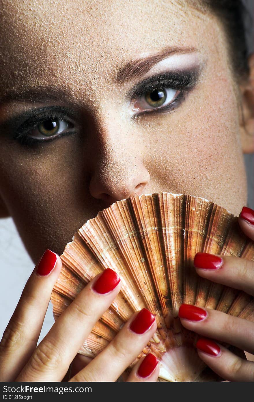 Beauty portrait of a young beautiful woman with sand on her skin and a shell. Beauty portrait of a young beautiful woman with sand on her skin and a shell