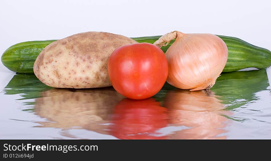 A potato, tomato, onion, and a cucumber reflected on aluminum foil. A potato, tomato, onion, and a cucumber reflected on aluminum foil