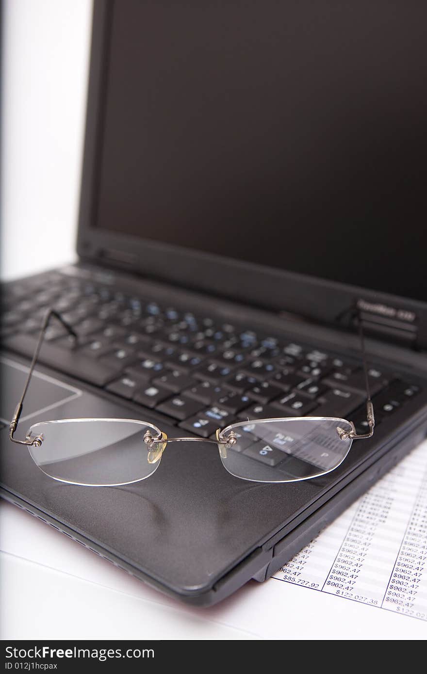 Black laptop, glasses, pen, sheet on the white background