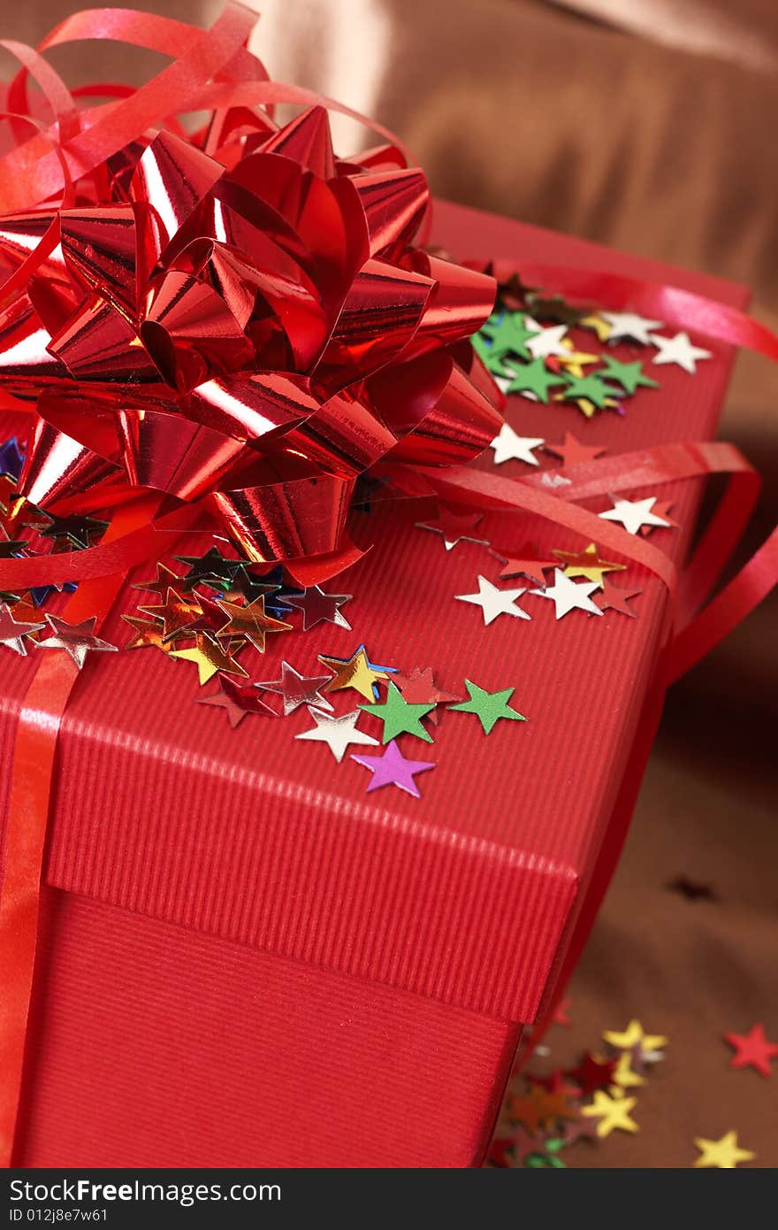 Red gift box with bows and stars on golden silk background